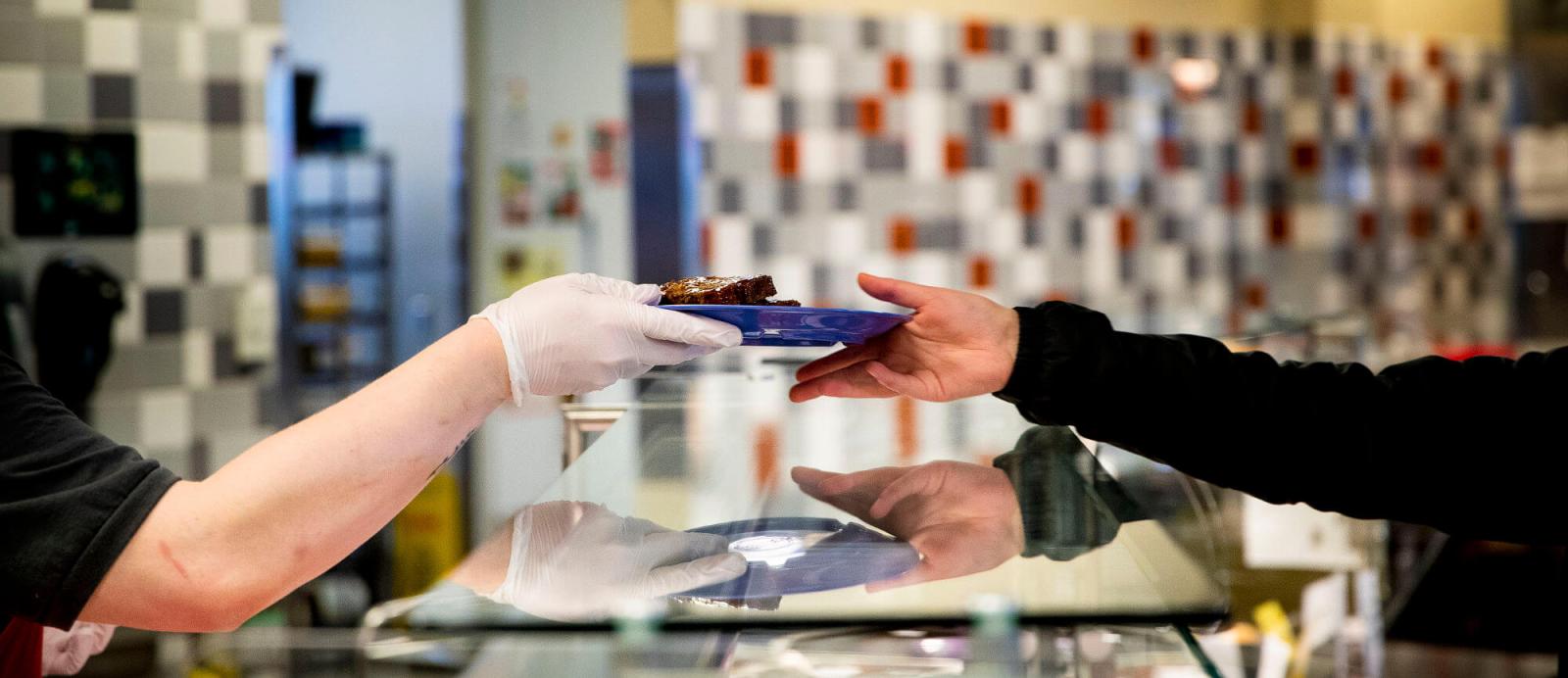 One person handing a plate of food to another over a counter