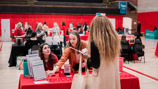 Two vendors pointing to their resources at their booth table and speaking with an employee at the wellness fair