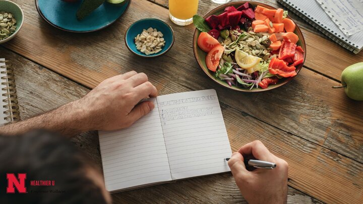 Person writing in notebook, next to a bowl of fresh vegetables