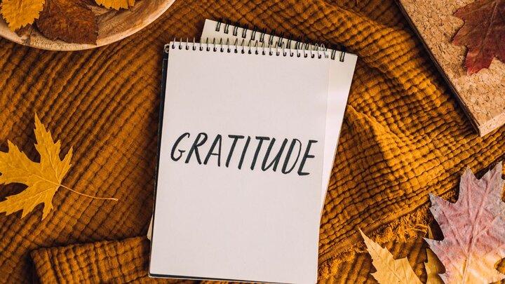 Notebook with the word gratitude written on it surrounded by leaves and orange towel