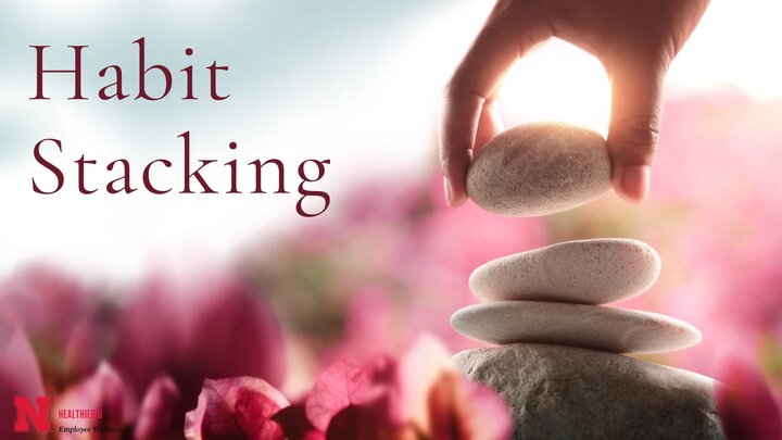 Person stacking rocks on top of one another in front of a pink and red leave background