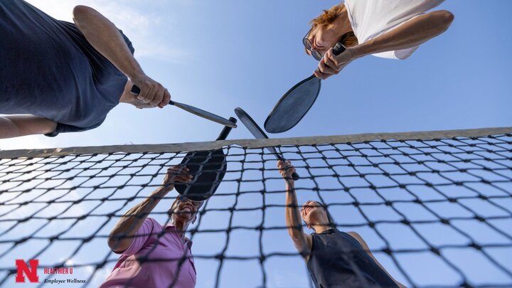 Four people over a pickleball net with their pickleball paddles